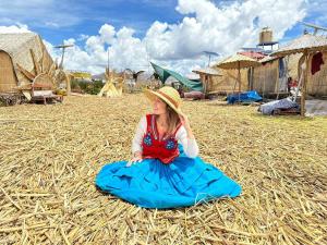 Una bambina con un vestito blu seduta su un fieno di Hotel - Titicaca Dora a Puno