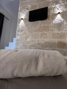 1 dormitorio con pared de piedra, 1 cama y TV en La PortaVecchia - #Home, en Monopoli