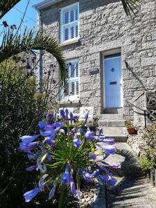 ein Steinhaus mit blauen Blumen davor in der Unterkunft Corvus - Beautiful cottage half a mile from Mousehole in Penzance