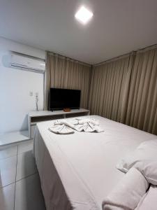 um quarto com uma cama branca e uma televisão em Mandara Lanai Apartamento Bangalô em Aquiraz