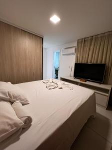 um quarto com uma grande cama branca e uma televisão de ecrã plano em Mandara Lanai Apartamento Bangalô em Aquiraz