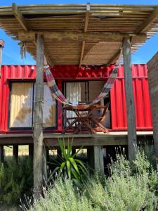 una casa roja con una hamaca en la cubierta en El Container de la Playa, en Punta del Diablo