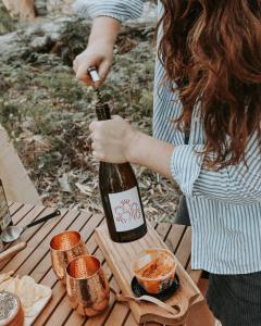 una mujer sosteniendo una botella de vino en una mesa de picnic en Numie - Freycinet Peninsula - Glamping en Coles Bay