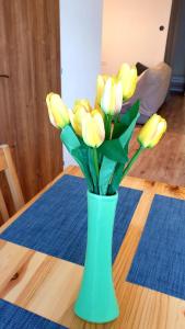 a green vase filled with yellow flowers on a table at Apartmán Bambuľka in Slovenská ľupča