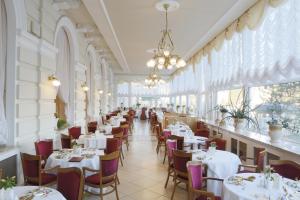 um restaurante com mesas e cadeiras brancas e janelas em Bristol Palace em Karlovy Vary