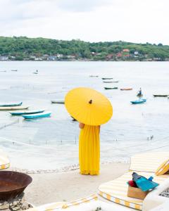 eine Person, die am Strand steht und einen gelben Regenschirm trägt in der Unterkunft Katoni Villa Lembongan in Nusa Lembongan