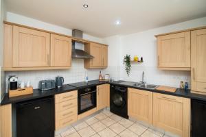 a kitchen with wooden cabinets and a black dishwasher at Pride Park House in Derby