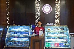 un hombre parado detrás de un mostrador con dos vitrinas de comida en Sky City Hotel Dhaka, en Dhaka
