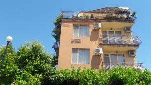 a tall yellow building with balconies and trees at Rooms Zora in Primorsko