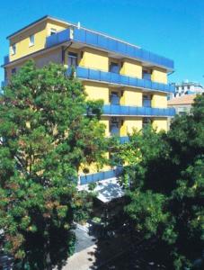 a tall yellow building with trees in front of it at Hotel Capitol in Pesaro