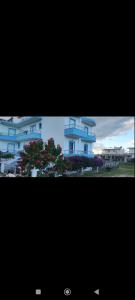 two pictures of a blue building with trees and flowers at KANALI HOLIDAYS APARTMENT in Kanali