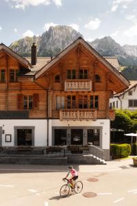 eine Person, die vor einem Holzgebäude Fahrrad fährt in der Unterkunft Hotel-Restaurant Valrose in Gstaad