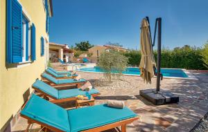 un patio con sillas azules y una sombrilla junto a la piscina en Cozy Home In Naselje Muzini With Wifi, en Tomišići