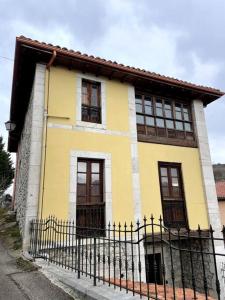 Ortiguero的住宿－La Llamera，黄色和白色的房子,有黑色的围栏
