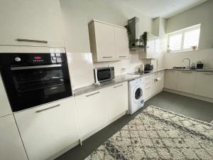 cocina con armarios blancos, lavadora y secadora en Central Mews House Altrincham en Altrincham