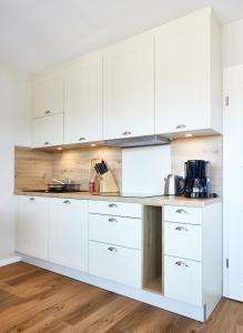 a white kitchen with white cabinets and a wooden floor at Ferienwohnung mit Seesicht Grimmershörnbucht in Cuxhaven