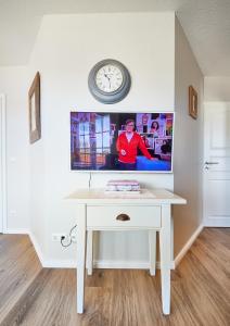 einen weißen Schreibtisch mit einem TV an der Wand und einer Uhr in der Unterkunft Ferienwohnung mit Seesicht Grimmershörnbucht in Cuxhaven