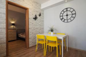 a dining room with yellow chairs and a table and a clock at KGHN Apartments Tkacka 28 in Szczecin