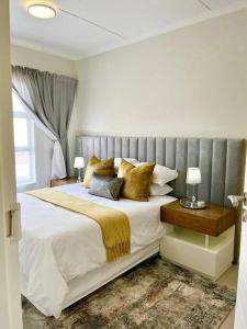 une chambre avec un grand lit blanc avec des oreillers dorés dans l'établissement 1 Harriet Place - Beautiful Self Catering 2 bedroom unit next to Carlswald Lifestyle Shopping Centre with free WiFi, Onsite Restaurant & Swimming Pool- Perfect for a small family in Midrand Carlswald, à Midrand