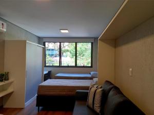 Zimmer mit 2 Betten, einem Sofa und einem Fenster in der Unterkunft Villa Leopoldina - Studios de aluguel por temporada no Moinhos de Vento in Porto Alegre