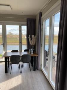 una sala da pranzo con tavolo, sedie e finestre di Tiny vakantiehuis aan het water met eigen steiger en airco a Kampen