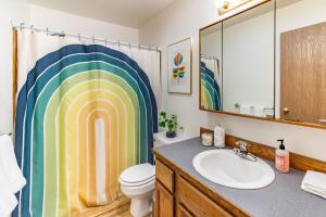 a bathroom with a sink and a toilet with a rainbow shower curtain at THE ROGUE WAVE-Beach Access, Ocean Views, Private in Kodiak