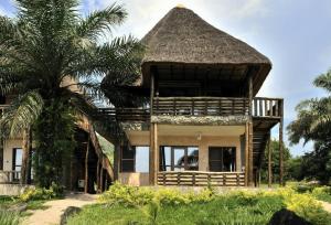 une maison avec un toit de chaume et un palmier dans l'établissement Tanganyika Blue Bay Resort, à Mugotora