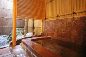 a bath tub in a room with a stone wall at Sennennoyu Koman in Toyooka