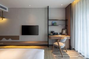een slaapkamer met een bureau en een televisie aan de muur bij Percent Hotel Yangshuo in Yangshuo