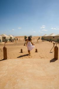 Una donna in abito bianco che cammina nel deserto di Beldi camp a Merzouga