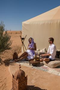 un hombre y una mujer sentados en una tienda en el desierto en Beldi camp, en Merzouga