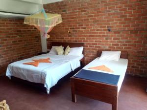 two beds in a room with a brick wall at Nimsara Homestay in Ella