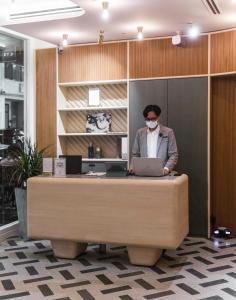 a person wearing a mask sitting at a desk with a laptop at KēSa House, The Unlimited Collection managed by The Ascott Limited in Singapore