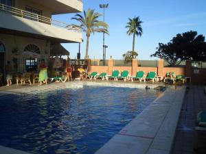 basen z zielonymi krzesłami i budynek w obiekcie Seafront apartment with open-air heated pool w mieście Fuengirola