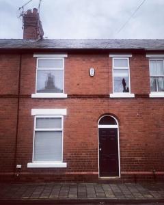 dom z czerwonej cegły z czarnymi drzwiami i psem w oknie w obiekcie Chester/Handbridge sleeps 6 with BT Sports & Pac-man w mieście Hough Green