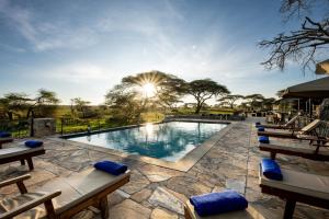 a large swimming pool with lounge chairs and the sun shining at Serengeti Sametu Camp in Serengeti National Park