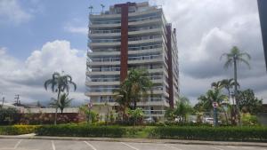 a tall building with palm trees in front of it at Doce Lar de Bertioga Frente ao Mar (Indaiá) in Bertioga