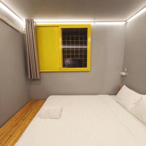 een kleine slaapkamer met een wit bed en een geel raam bij Hanowood Homestay in Hanoi