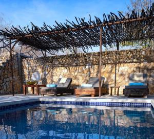 una piscina con 2 sillas y una pérgola en Gwango Elephant Lodge en Dete