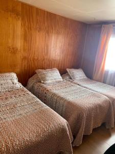 two beds in a room with wooden walls at Cabañas Bosque Sur in Puerto Varas