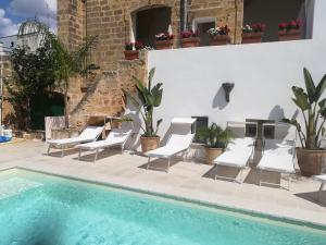 una piscina con sillas blancas y una mesa y un edificio en Dimora Maltese, en Morciano di Leuca