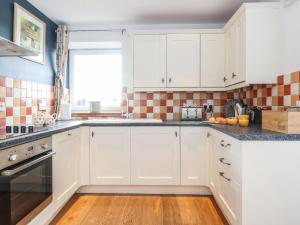 una cocina con armarios blancos y una ventana en Grey Craig Cottage, en Lockerbie