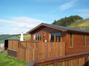 uma casa de madeira com uma cerca e uma colina em Skylark Lodge with Hot Tub em Cupar