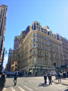 ein großes Gebäude an einer Stadtstraße mit Leuten, die die Straße überqueren in der Unterkunft NYC Empire Apartments in New York