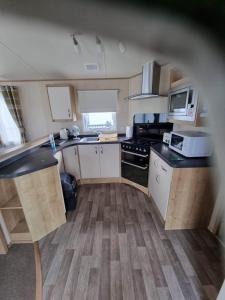 una pequeña cocina con armarios blancos y encimeras negras en Caravan L16, en Mablethorpe