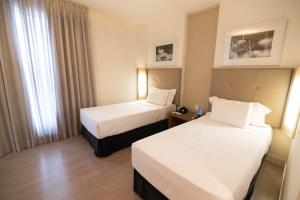 a hotel room with two beds and a window at H2 Platinum Lourdes in Belo Horizonte