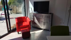 un salon avec une chaise rouge et une télévision dans l'établissement Domaine de L'Outarde Canepetiére Gîte A, à Aigues-Mortes