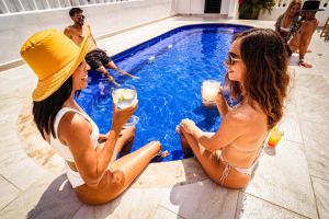 two women sitting next to a swimming pool with drinks at Nomads Party Hostel in Cancún