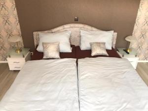 ein Bett mit weißer Bettwäsche und Kissen darauf in der Unterkunft Pension Alice in Apfelstädt