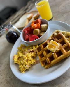 a plate of breakfast food with waffles and a bowl of fruit at Hotel Casa San Juan in Managua